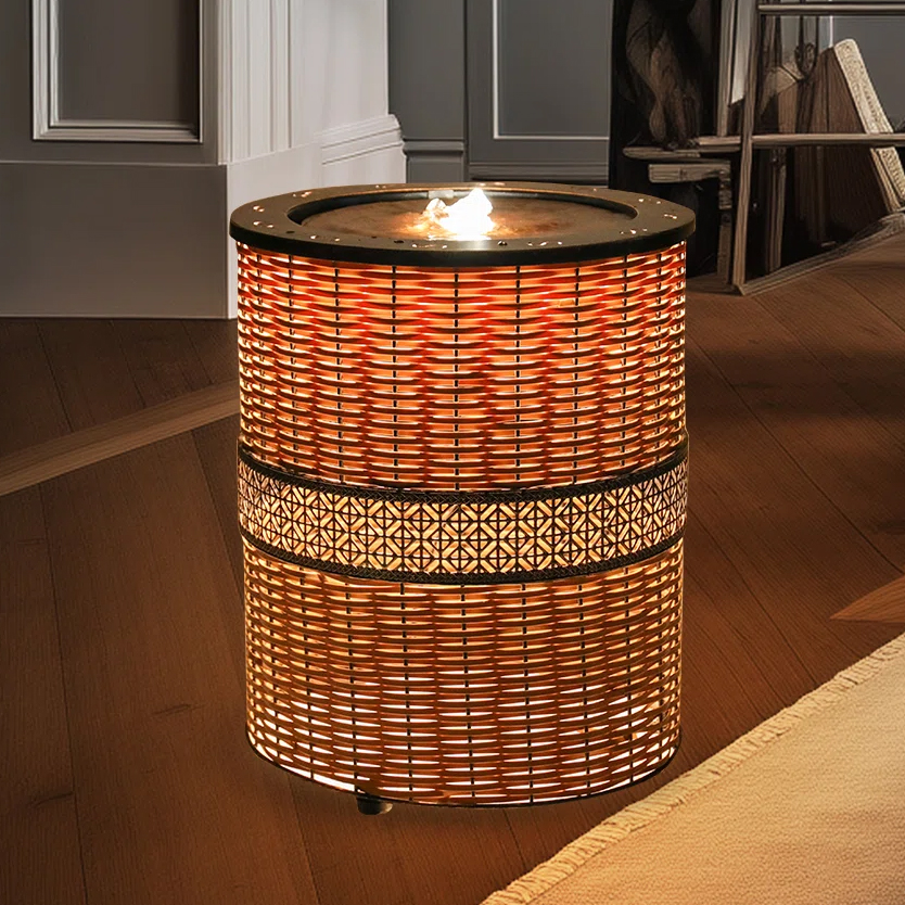 A cylindrical wicker-style lamp with a decorative pattern and a flame-like light source on top, placed on a wooden floor in a dimly lit room.