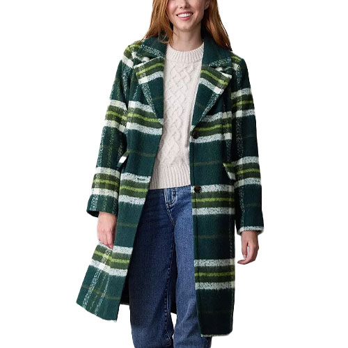 A woman wearing a green and white plaid coat over a beige cable-knit sweater and blue jeans.