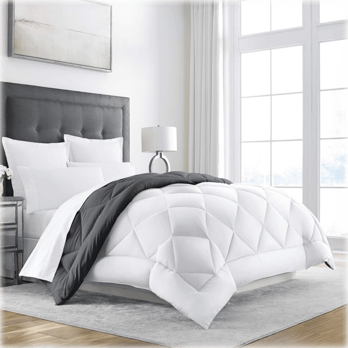A white and gray comforter set on a bed with a tufted headboard, flanked by a nightstand and lamp.