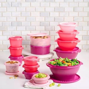 Various sizes of pink and purple food storage containers with some containing food such as salad and grapes.