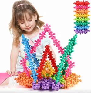 Three sets of colorful interlocking building blocks are arranged in rising towers, with a child sitting beside them.