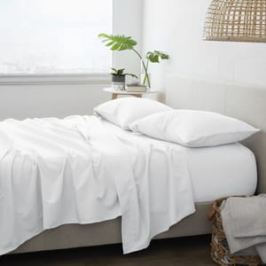 A 4-piece queen sheet set featuring white sheets with a smooth and soft appearance. Includes a fitted sheet, flat sheet, and two pillowcases, placed on a neatly made bed in a bright room with a beige headboard and modern decor elements.