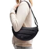 A person is wearing a black, crescent-shaped shoulder bag from Got Bag made of quilted material, paired with a light, ribbed sweater and light-colored pants.