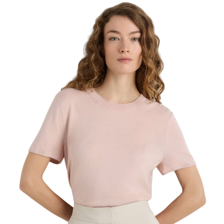 A person wearing a light pink short-sleeve knitted top with a round neckline, paired with cream-colored pants, standing against a neutral background.