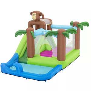 Inflatable bounce house with a tropical theme, featuring a monkey design, palm trees, a slide, and a small pool area.