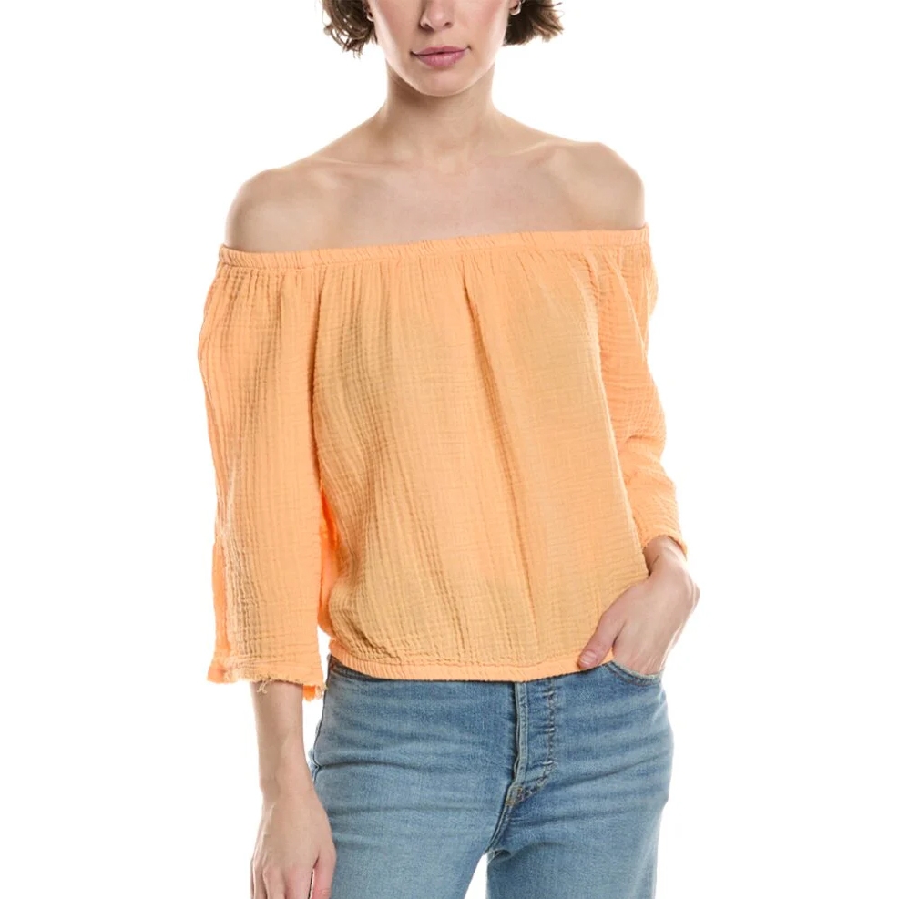 The Michael Stars Isabel Convertible Top is a lightweight, off-the-shoulder blouse in a soft peach color. It features three-quarter sleeves and a relaxed fit, paired with blue jeans.