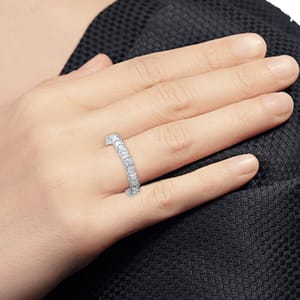 A hand is adorned with a diamond eternity ring placed on the ring finger, featuring a row of rectangular cut stones set in metal.