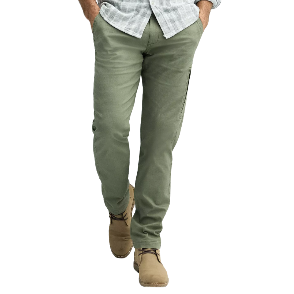 A man wearing olive green pants, a light gray checkered shirt, and beige suede shoes, hands in pockets.