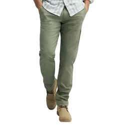 A man wearing olive green pants, a light gray checkered shirt, and beige suede shoes, hands in pockets.