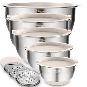 Four stainless steel mixing bowls with lids are stacked, paired with three grating attachments; all feature a brushed exterior finish.
