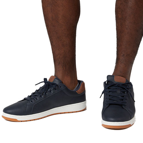 A pair of navy blue sneakers with brown accents and white soles, shown on a person’s feet.