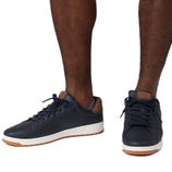 A pair of navy blue sneakers with brown accents and white soles, shown on a person’s feet.