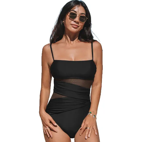 A woman wears a black one-piece swimsuit with spaghetti straps and a mesh midsection, accessorized with sunglasses and a bracelet.