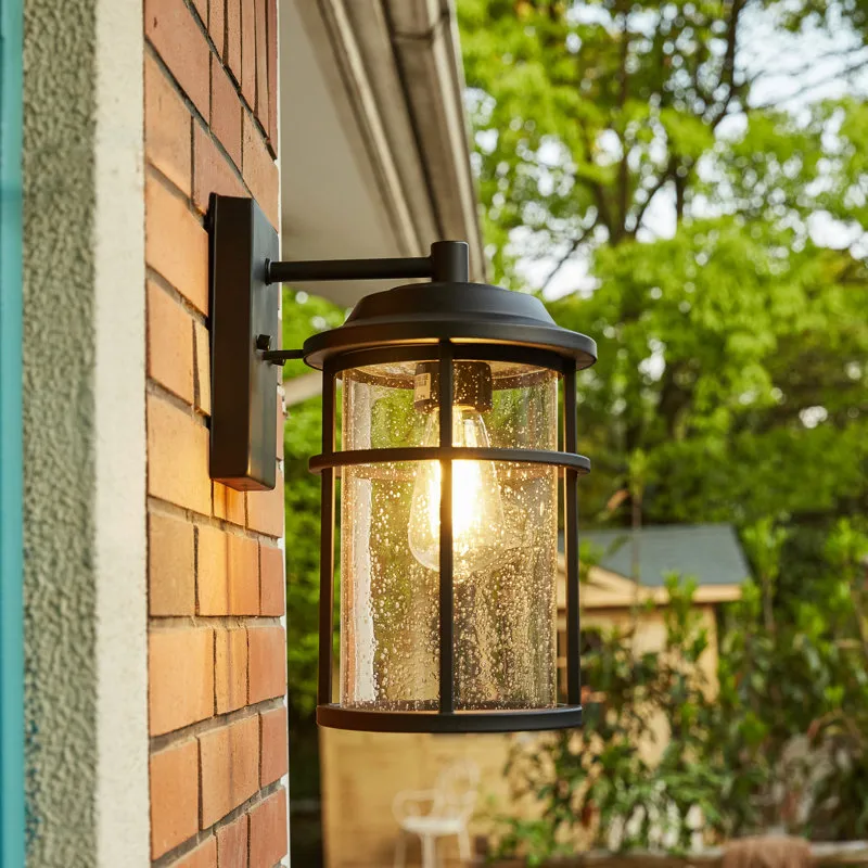An outdoor wall-mounted lantern with a black metal frame and clear glass, installed on a brick wall, provides ambient lighting.