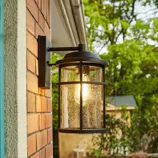 An outdoor wall-mounted lantern with a black metal frame and clear glass, installed on a brick wall, provides ambient lighting.