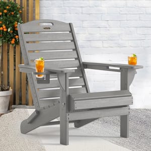 A gray Adirondack chair with armrests featuring integrated cup holders, each holding a glass with an orange beverage. It is set against a white brick wall with potted plants nearby.
