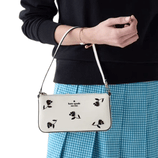 A person holds a small white handbag with a floral print and \“kate spade\“ logo, paired with a blue checkered skirt and a simple bracelet.