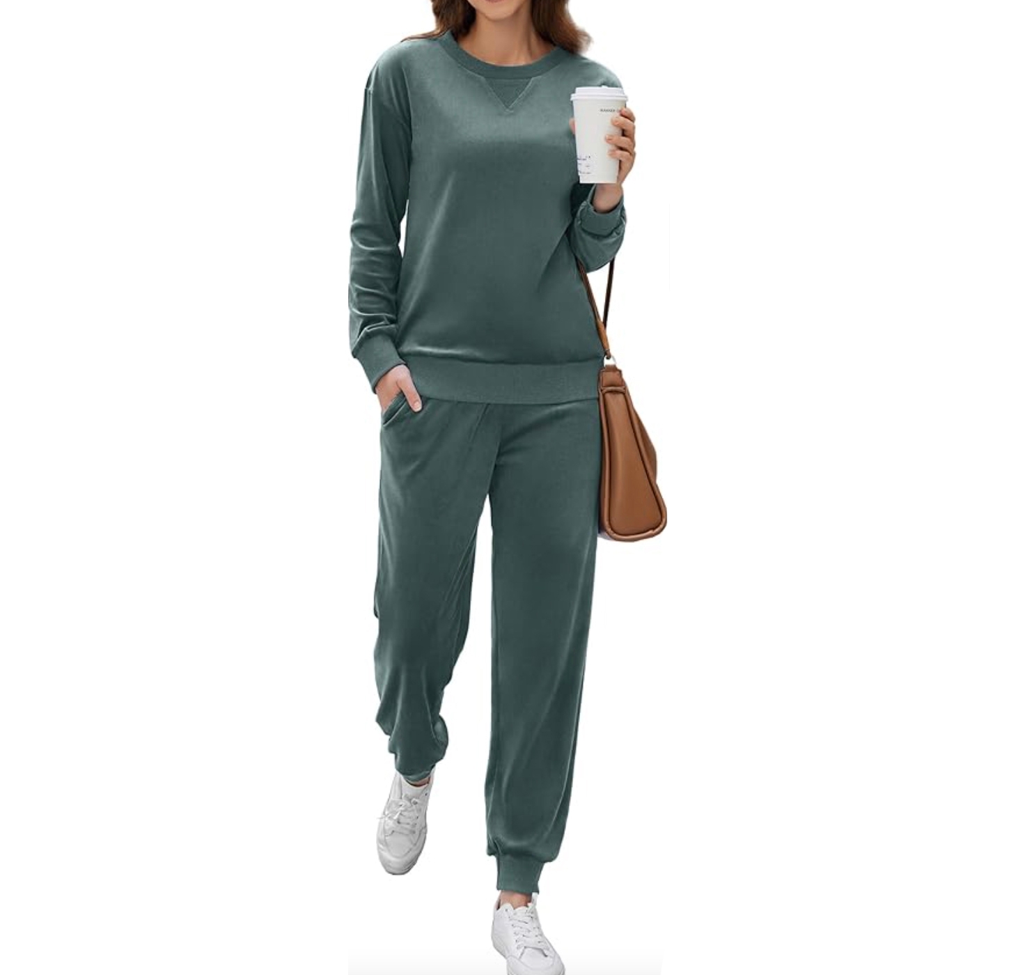 A green two-piece loungewear set consisting of a long-sleeve sweatshirt and jogger pants with pockets. The outfit is paired with white sneakers and a brown shoulder bag. The person holds a coffee cup.