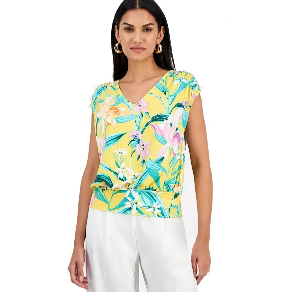 Woman wearing a yellow floral blouse with a V-neck and short sleeves, paired with white pants.