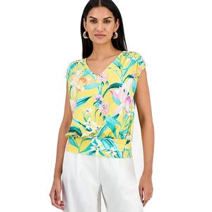 Woman wearing a yellow floral blouse with a V-neck and short sleeves, paired with white pants.