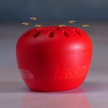 Red fruit fly trap device labeled \“TERRO\“ with small perforations, shown to attract and trap adult fruit flies, with bananas in the background.