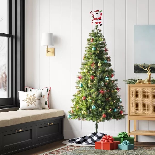 Decorated Christmas tree with colorful ornaments and a reindeer topper, accompanied by wrapped gifts on the floor.