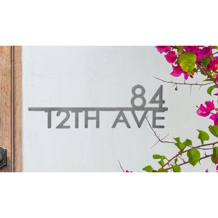 Modern house number sign displaying \“84 12TH AVE\“ in sleek metal, mounted on a wall with pink bougainvillea flowers nearby.