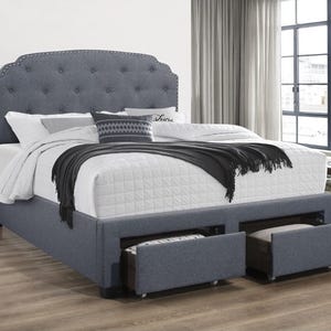 A bed with a tufted headboard upholstered in blue fabric features built-in storage drawers under the mattress and a white quilt with black accents.