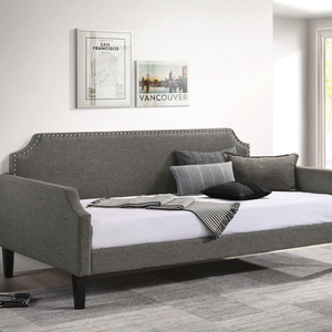 A gray upholstered daybed with nailhead trim features a curving backrest, bolster and square pillows, set against a wall with framed city posters.
