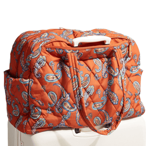 Quilted orange duffle bag with a paisley pattern resting on top of a suitcase, featuring sturdy handles and side pockets.