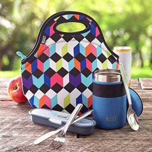 The 7pc Insulated Food Travel Kit includes a colorful geometric-patterned lunch bag, a blue insulated food jar, a utensil case with fork, knife, and spoon, and a drink can. The set is designed for efficient food storage and portability.