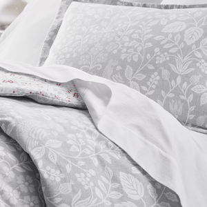 A set of bedding featuring a light gray and white floral pattern with decorative leaves and berries, paired with plain white sheets for contrast.