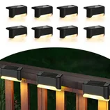 A set of black solar-powered LED deck lights designed for outdoor use is shown mounted on a wooden railing, providing warm downward lighting.