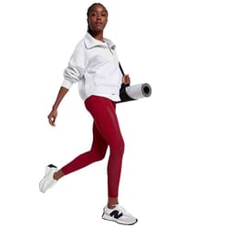White Calia Scuba 1/4 Zip Pullover with a relaxed fit, featuring a high collar and long sleeves, paired with red leggings. The outfit is complemented by white sneakers and a yoga mat slung over the shoulder.