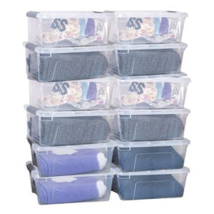 A stack of clear plastic storage boxes with lids, each containing folded clothes, including jeans, shirts, and socks.