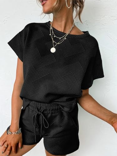 A woman is wearing a black textured short-sleeve top with matching drawstring shorts, accessorized with layered necklaces and hoop earrings.