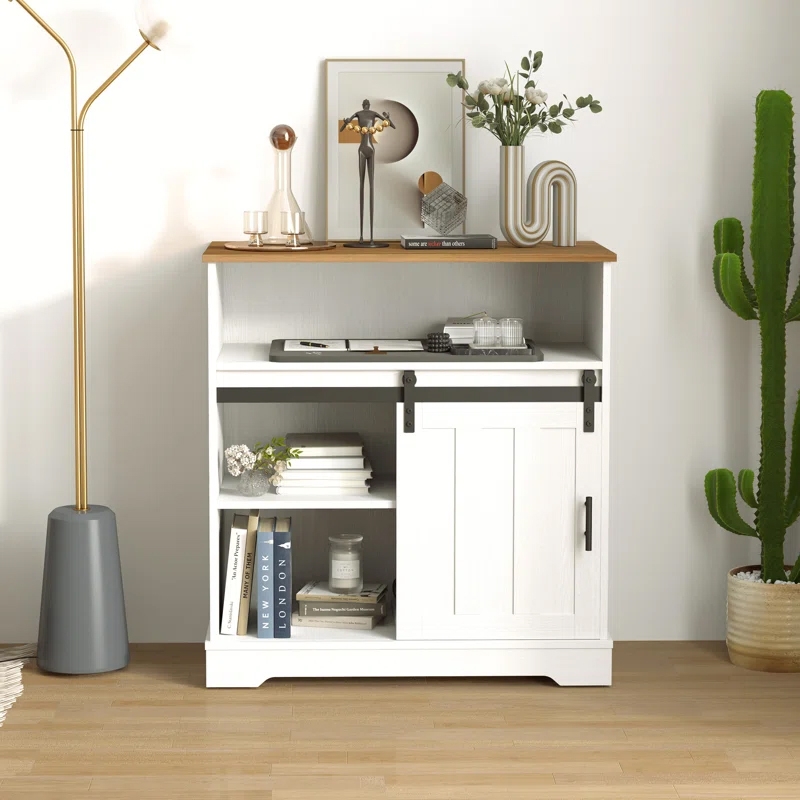 A white entry cabinet with a sliding door, an upper wooden shelf, and several open compartments filled with books and decor items, placed next to a cactus and under a floor lamp.