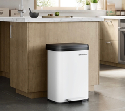 A white trash can with a black lid is located in a modern kitchen with wooden cabinets and a white countertop.