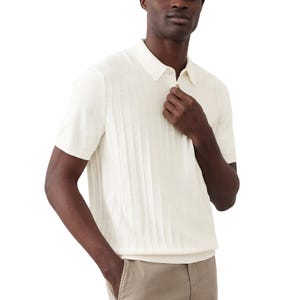 A man is wearing a light-colored, short-sleeve knit polo shirt with a ribbed texture, paired with beige pants.