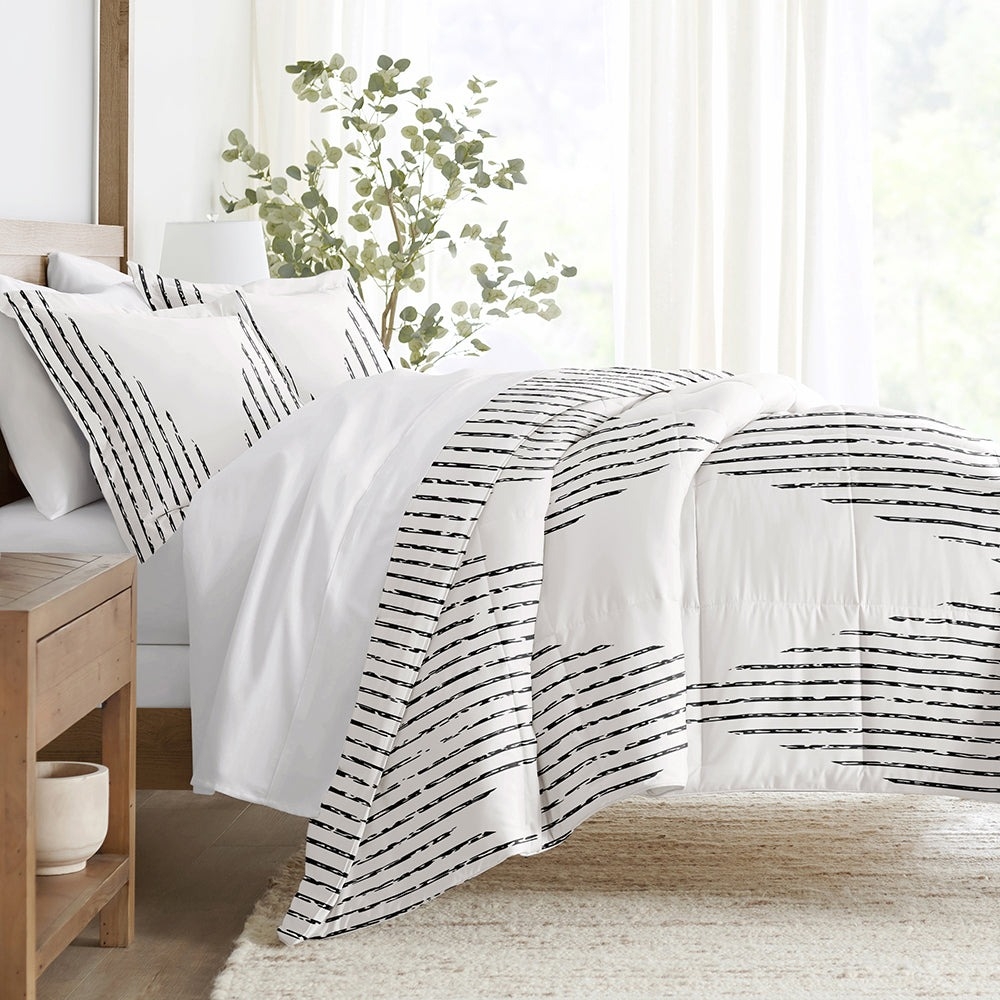 A bedding set featuring a white comforter and pillowcases with black, abstract striped patterns, displayed in a bright, minimalist bedroom setting.