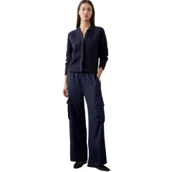 A woman is dressed in a dark blue textured cardigan and wide-leg satin cargo pants, paired with black pointed flats.