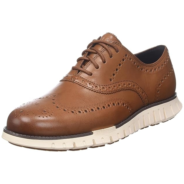 A brown leather wingtip oxford shoe with brogue detailing and a contrasting white rubber sole.