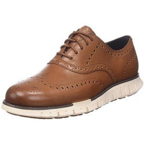 A brown leather wingtip oxford shoe with brogue detailing and a contrasting white rubber sole.