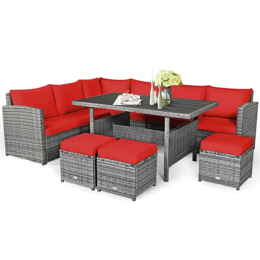 Outdoor gray rattan patio dining set with red cushions, featuring a corner sofa, rectangular table, and three ottomans.