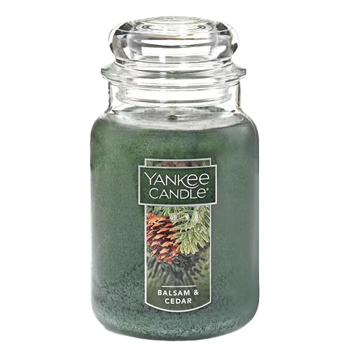 A Yankee Candle in the \“Balsam & Cedar\“ scent featuring a green color and a picture of pinecones and cedar branches on the label, housed in a classic glass jar with a lid.