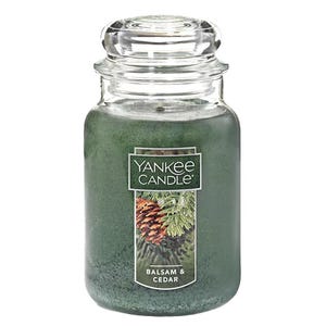 A Yankee Candle in the \“Balsam & Cedar\“ scent featuring a green color and a picture of pinecones and cedar branches on the label, housed in a classic glass jar with a lid.