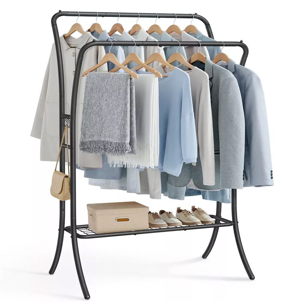 A double-rod clothes rack featuring two tiers for hanging clothes, includes wooden hangers with a mix of coats, shirts, and scarves. The lower shelf holds a box and shoes, and a small beige bag hangs on the side. The frame is dark metal.