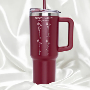 A maroon travel mug with a handle and straw features floral designs and the text \“NANA'S GARDEN,\“ accompanied by names written vertically alongside each flower illustration.