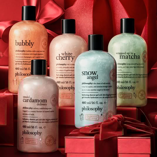 Five Philosophy hydrating shower gels in various scents: Bubbly, White Cherry, Wrapped Up in Matcha, Snow Angel, and Special Cardamom Delivery, 480 ml each, set against a red backdrop with ribbons.