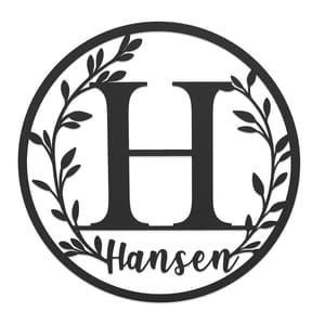 A circular monogram sign featuring a large letter \“H\“ surrounded by a leafy wreath design, with the name \“Hansen\“ written below in a script font.